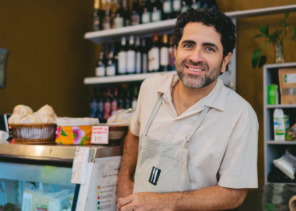 Un comerciante latino sonriendo detrás del mostrador de su negocio