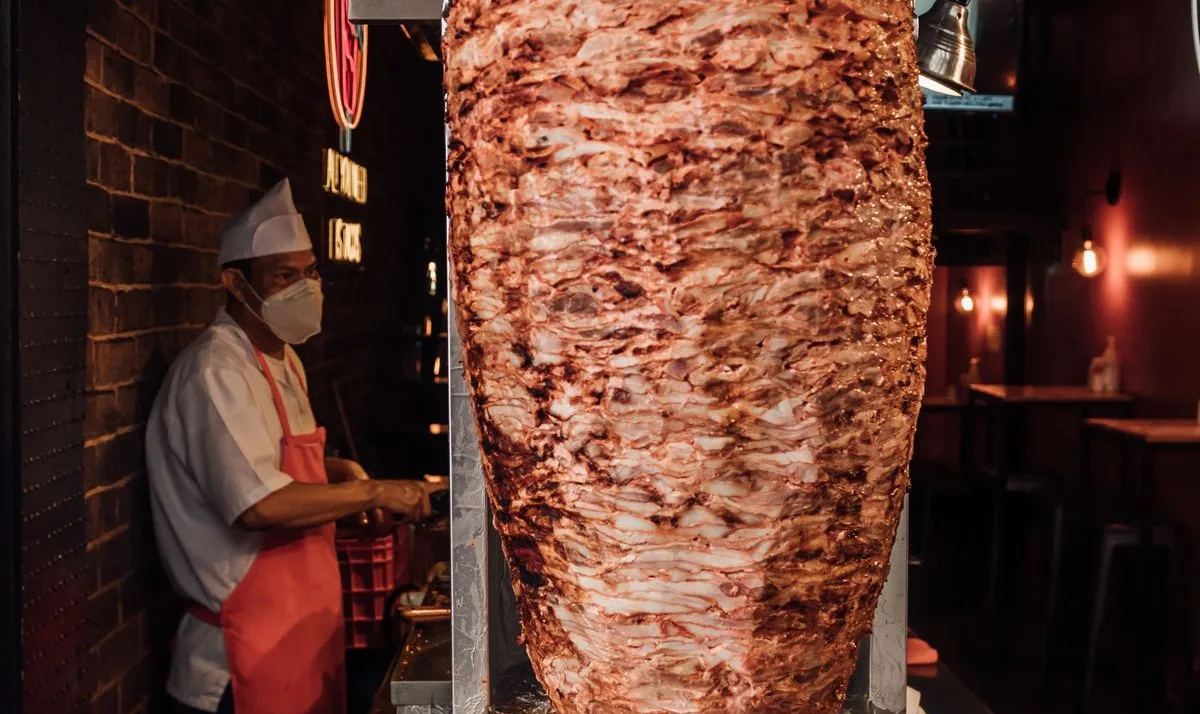 Un taquero junto a su trompo al pastor en una taquería